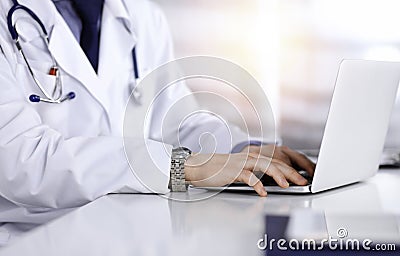 Unknown male doctor sitting and working with laptop in a darkened clinic, glare of light on the background, close-upof Stock Photo