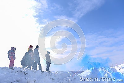 An unknown man squats next to four children in winter in a fog in the sun looking at the colored blue smoke Editorial Stock Photo