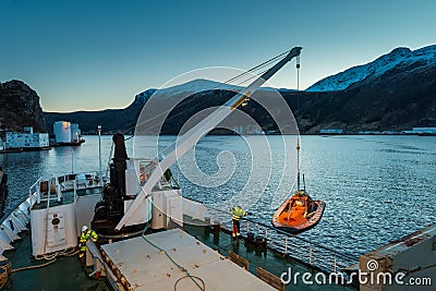 Unloading cargo with crane from freighter in the port of the city Maloy in Norway seen from cruise ship in early morning Stock Photo