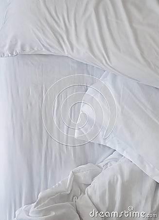 Unmade bed close-up with white bedsheet and pillows. Stock Photo