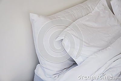 Unmade bed close-up with white bedsheet and pillows. Stock Photo