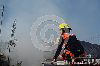 Unmarried Woman Fire Fighter With Protective Hat sitting on top of fire truck in the area of burning house Editorial Stock Photo