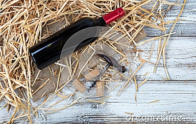 An unopen bottle of red wine plus corkscrew on top of straw and Stock Photo