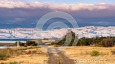 Unpaved road on the shorelines of South San Francisco Bay Area; dramatic sunset clouds covering the Diablo Mountain Range visible Stock Photo