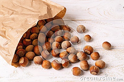 Unpeeled hazelnuts spilled out of a paper bag onto the white wood table. Nuts as an antioxidant and protein source for ketogenic Stock Photo