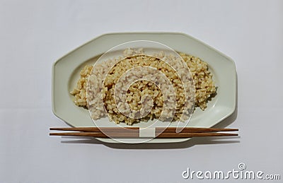 Unpolished brown rice on a white plate with chopsticks Stock Photo