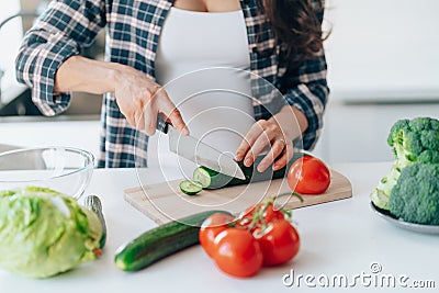 unrecognisable pregnant woman cook salad cutting cucumber on wooden board putting fresh vegetables and fruit on table in Stock Photo