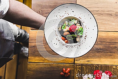 Unrecognisable waiter serving black tagliolini pasta dish with shrimp and tomatoes on white minimalist plate. Italian Stock Photo