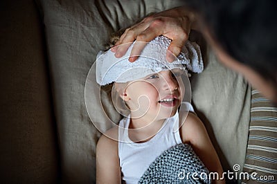 Unrecognizable father checking on small sick son lying in bed indoors at home. Stock Photo