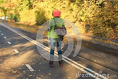 Unrecognizable girl with her back on roller skates rides in the autumn in park along the paths among fallen leaves. Editorial Stock Photo