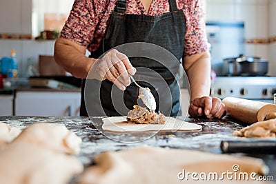 Unrecognizable Latin Elderly Woman Putting Chilean Meat and Onion-filled Empanadas in her Countryside Home Kitchen Stock Photo