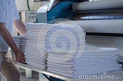 Unrecognizable man stacking freshly ironed sheets or fabrics in an industrial laundry Stock Photo