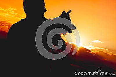 Unrecognizable person holding a dog. Silhouette against sundown Stock Photo