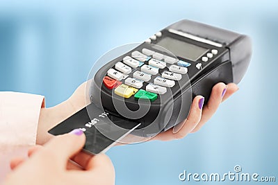 Unrecognizable woman holds swiping machine and credit card, pays for purchase, uses bank terminal in shop, isolated over blue back Stock Photo