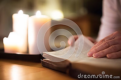 Unrecognizable woman reading Bible. Burning candles next to her. Stock Photo