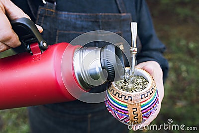 unrecognizable woman serving mate with a red thermo, in a colorful ethnic mate. Stock Photo