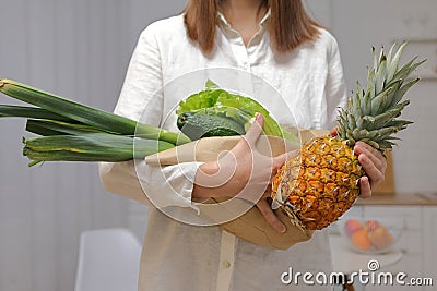 Unrecognizable woman wearing white shirt preparing to cook lunch holding avocado pineapple leek green lettuce leaves in light Stock Photo