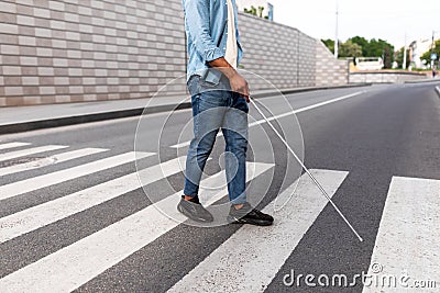 Unrecognizable young black visually impaired man with cane walking across city street, closeup Stock Photo