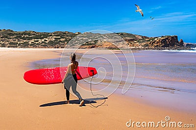 Unrecognizable young woman carrying surf board at Praia da Bordeira, Portugal. Young woman holding surf board on the sea shore. Editorial Stock Photo