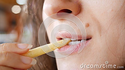 Unrecognizable young woman is eating french fries in fast food restaurant. She is holding one hand potato, mouth closeup Stock Photo