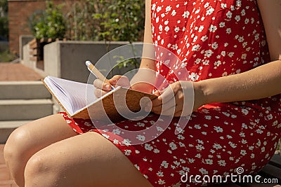 Unrecognizable Young woman in red dress Writing Gratitude Journal on wooden bench. Today I am grateful for. Self Stock Photo