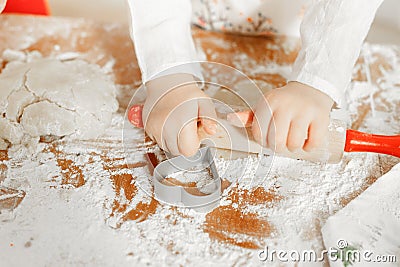 Unrecongnizable small child rolls up pastry with rolling pin, surrounded with cookie cutter in form of heart, going to Stock Photo