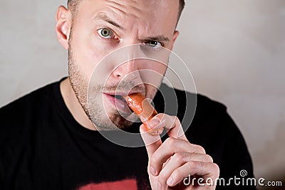 Man eating a sausage, holding it with his hand Stock Photo