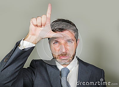 Unshaven sad and ashamed businessman crying doing loser sign with hand and fingers on his forehead with funny depressed expression Stock Photo