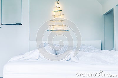 Unusual Christmas tree made of wooden sticks with a garland on the white wall above the bed . Simple, minimal conscientious Stock Photo