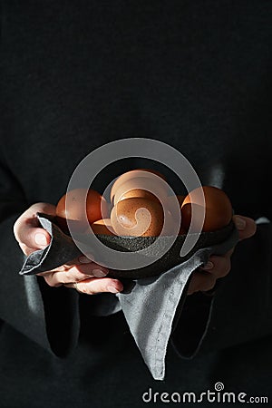 Unusual Easter on a dark background. A bowl of brown eggs with hands Stock Photo