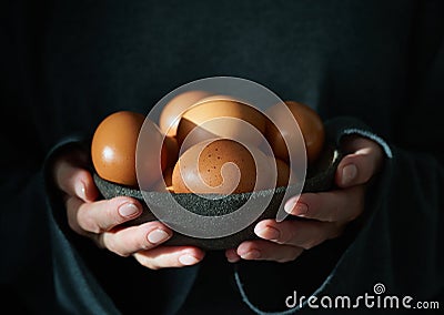 Unusual Easter on dark background. Bowl of brown eggs with hands Stock Photo