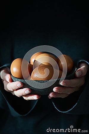 Unusual Easter on dark background. Bowl of brown eggs with hands, vertical Stock Photo