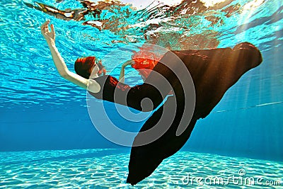 Unusual girl drowns in the pool. A girl with red hair and a dress falls to the bottom of the pool on the background of Stock Photo