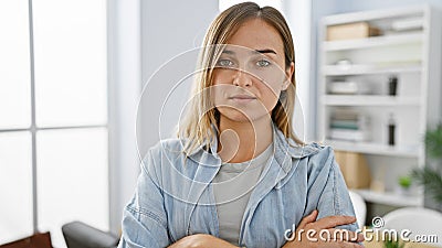 Unwavering young blonde business woman, a picture of serious concentration, stands with arms crossed in the vibrant office Stock Photo