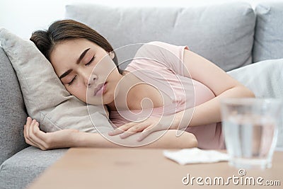 Unwell condition young Asian girl sleeping on sofa after checking temperature and taking medicines and water, Health and illness Stock Photo