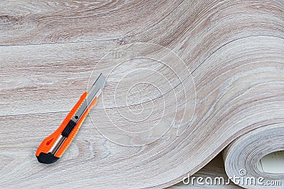 Unwound roll beige linoleum with wood texture and construction knife for cutting Stock Photo
