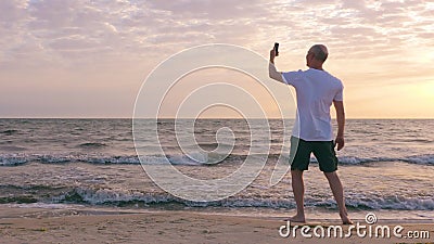 Uomo adulto che rende a selfie alba andmobile di mattina della foto sulla spiaggia del mare stock footage Uomo adulto che rende a selfie alba andmobile di mattina della foto sulla spiaggia del mare stock footage
