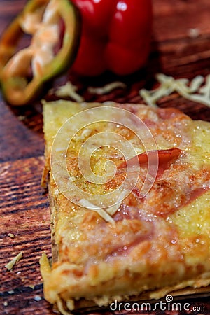 Up-close half pizza slice with ham, salami and cheese on wooden background with fresh ingredients on top Stock Photo