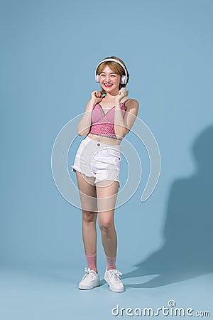 Upbeat positive Asian girl enjoys every bit of music wears stereo headphones on her ears holds a mobile phone listens to favorite Stock Photo