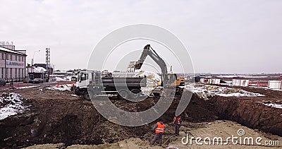 Upper aerial shot: a tractor bucket fills the truck body. An excavator and a truck load the ground. Flight over the Editorial Stock Photo
