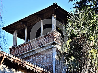 Upper part, immersed in the blue sky, of a tower with small columns and a palm tree in Padua. Stock Photo