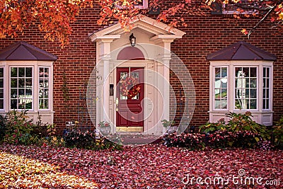Upscale brick home with bay windows and columns in auturm with leaves covering the front yard and bushes and a no soliticting sign Stock Photo