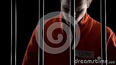 Upset arrested man in orange suit behind prison bars, death penalty judgment Stock Photo