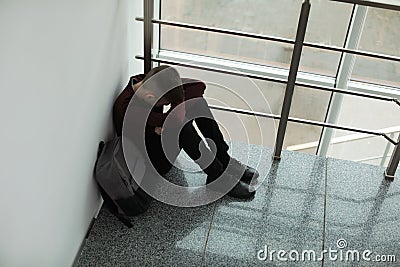 Upset boy with backpack sitting near window indoors Stock Photo