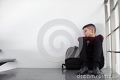 Upset boy with backpack sitting on staircase indoors Stock Photo