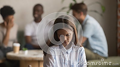 Upset bullied young girl sitting alone excluded by bad friends Stock Photo