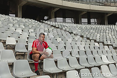 Upset Caucasian male rugby player sitting with rugby ball in stadium Stock Photo