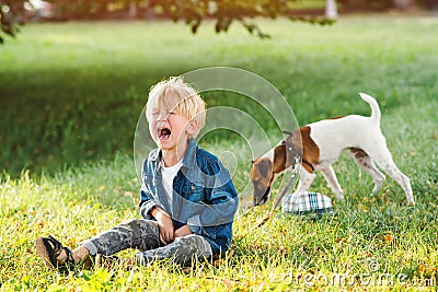 Upset child boy at the summer park. Childhood. Sad kid walking with dog. Little boy crying and sitting on the ground Stock Photo