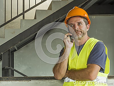 Upset construction worker or stressed contractor man in hardhat and vest talking on mobile phone unhappy in stress messing with Stock Photo