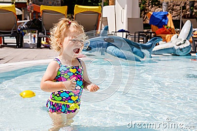 Upset crying little toddler girl in the swimming pool on family vacations in a hotel resort. Sad child playing in water Stock Photo